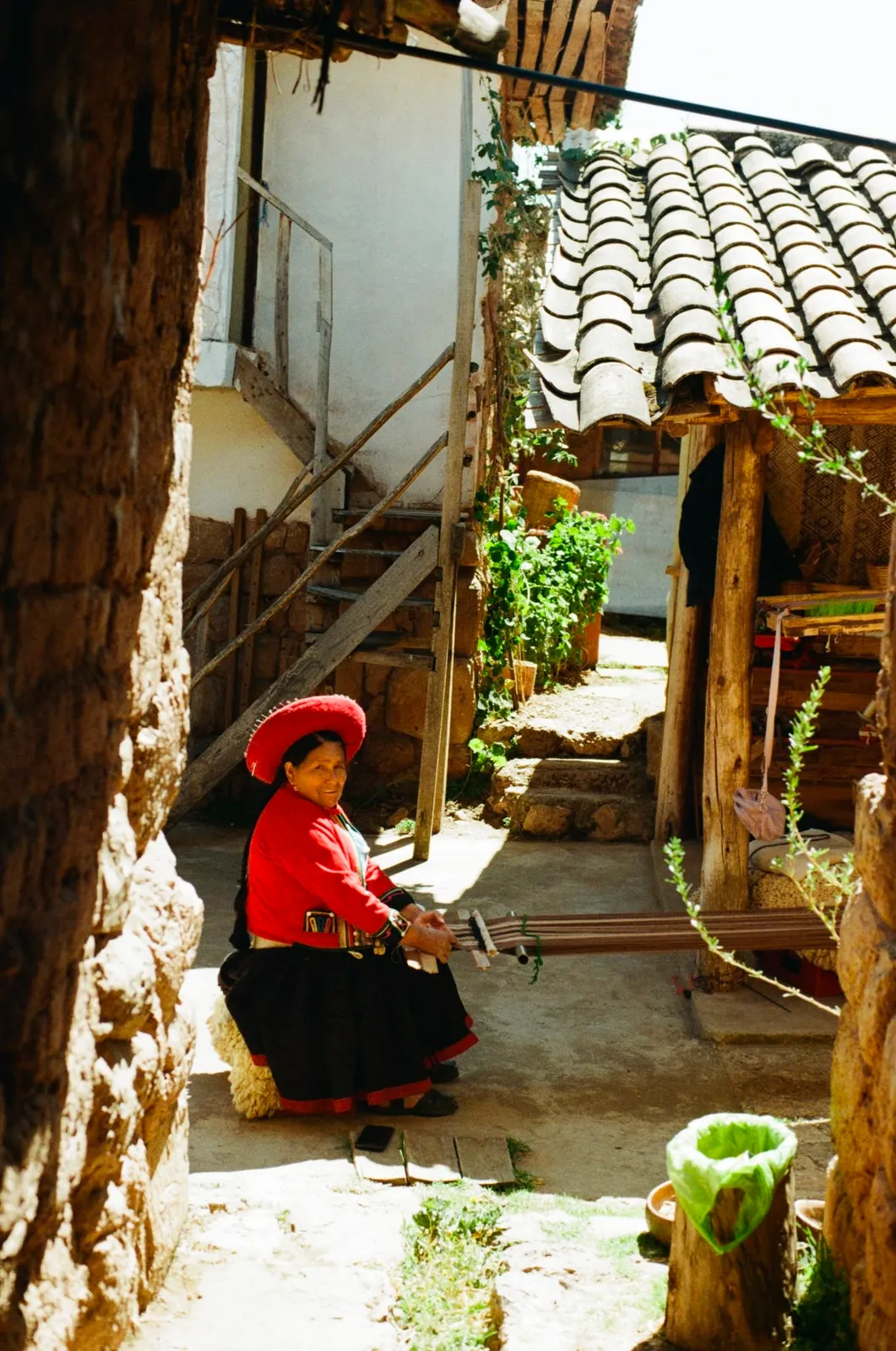 Weaver in a red hat working at a backstrap loom in the courtyard