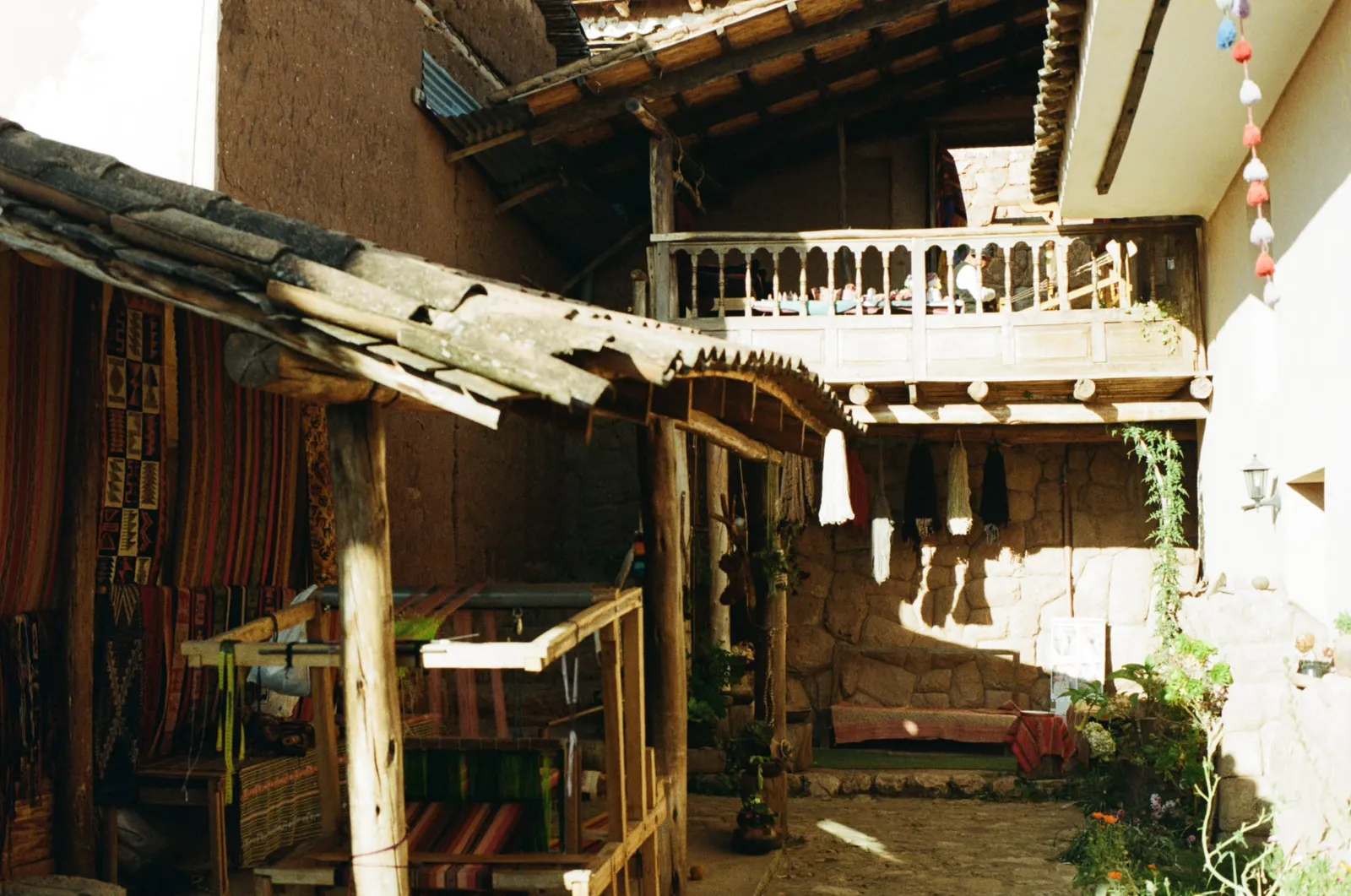Workshop courtyard with looms, hanging skeins and a wooden balcony