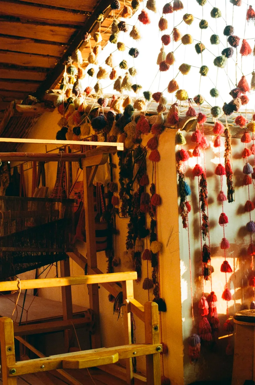 Colourful wool pompoms hanging beside a loom