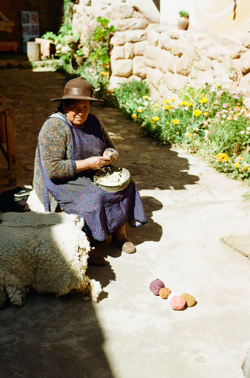 Artisan seated in the courtyard preparing materials beside a fleece and dyed balls of yarn