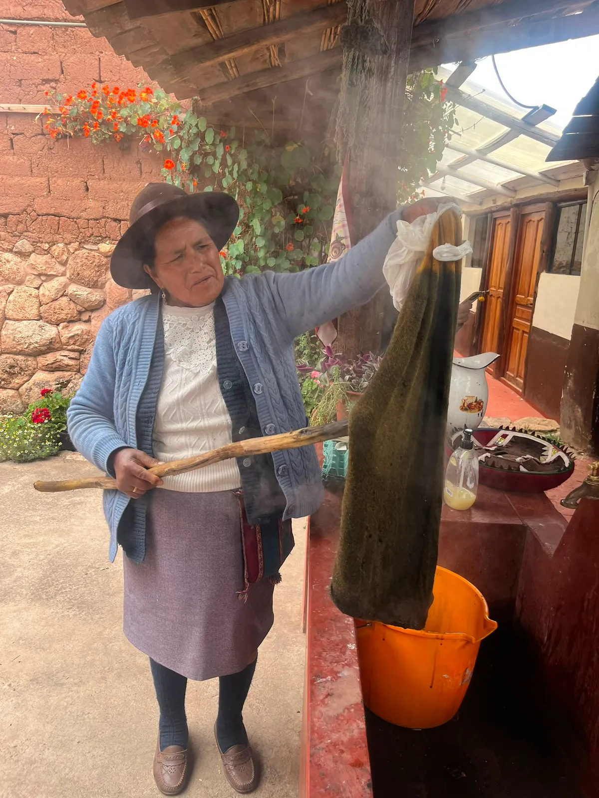 Artisan lifting a freshly dyed skein of wool over a bucket, in the steam